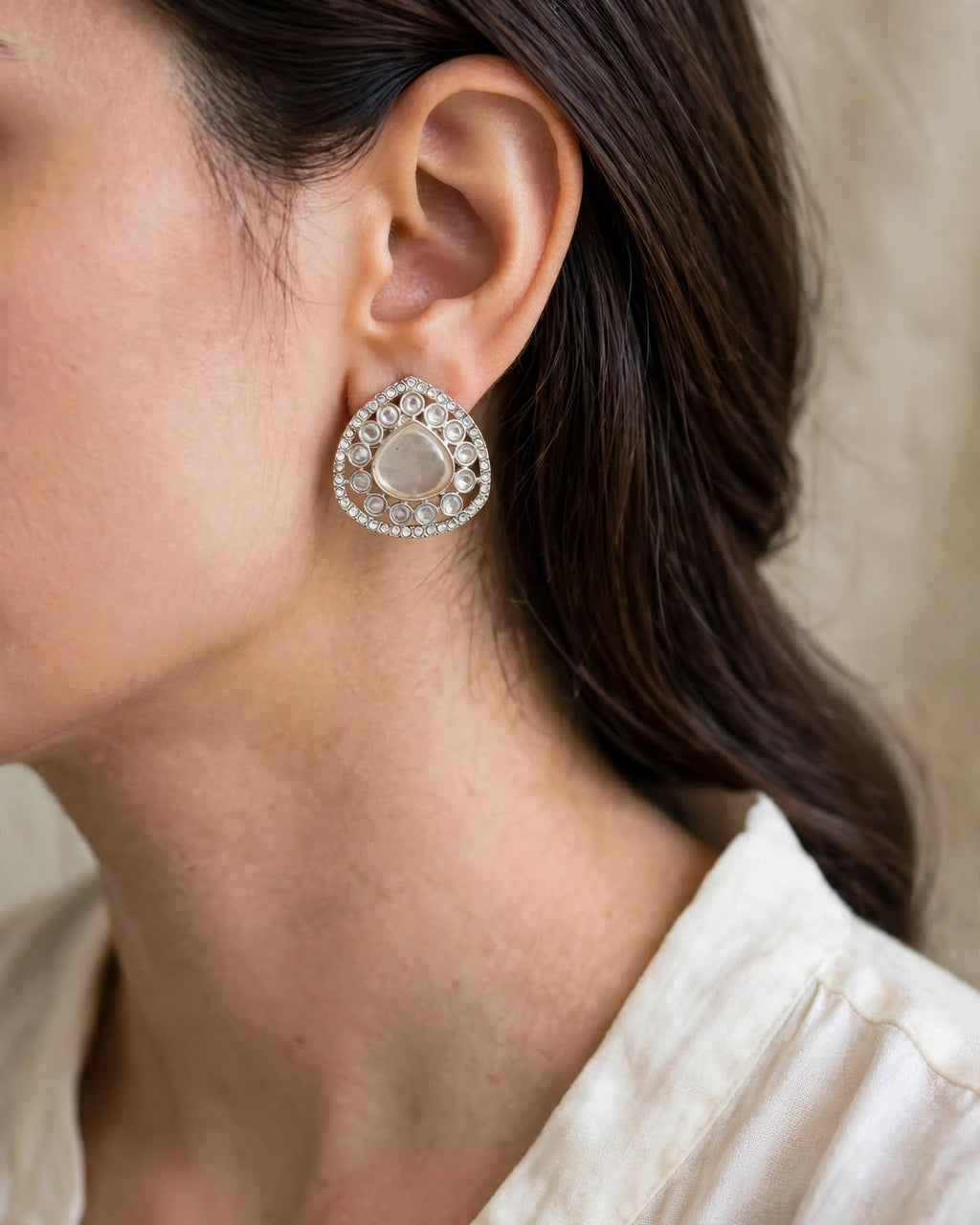 Milky white teardrop earring with clear accents and a silver-tone border worn on the ear